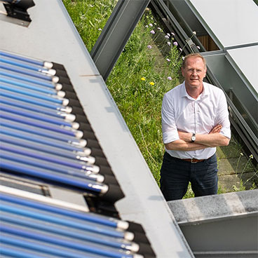 Prof. Dr. Lang steht auf einem bepflanzten Dach zwischen Solarpanels.